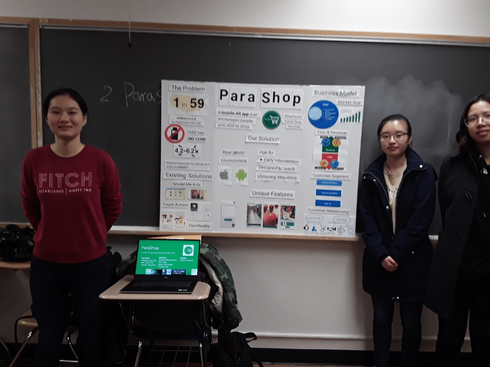 Three young women, Nan Chen, Mengting Xia, Yuemin Tang, stand in front of a classroom with a large poster demonstrating their app: Parashop