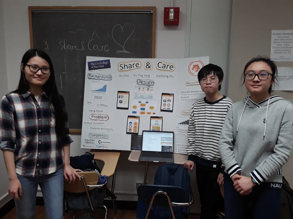 Three students stand in a classroom in front of a tri-fold board presenting their app: Share & Care.