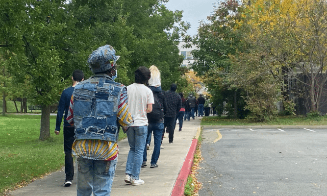 A group of people in line on a sidewalk beside a road