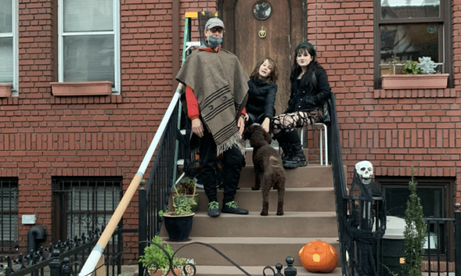 A man. woman, middle school-aged child and dog gather together on the steps leading to their home or apartment.