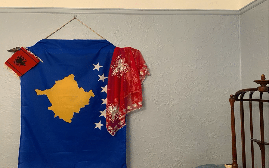 The Albanian (red) and Kosovo (blue) flags are shown hanging on the wall.  