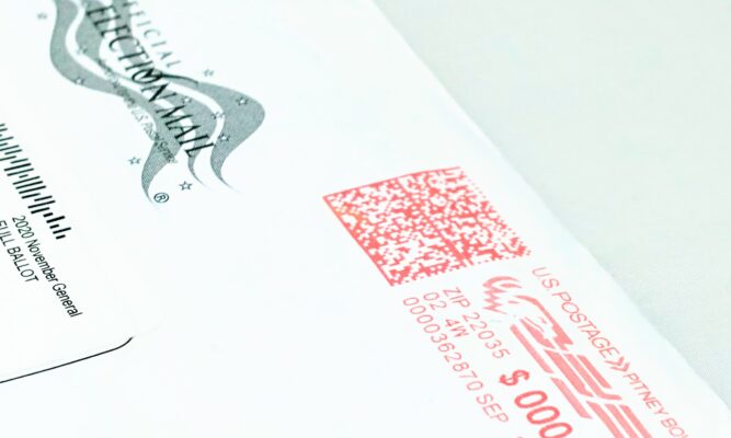 The corner of a white envelope that is postmarked and marked as Official Election Mail