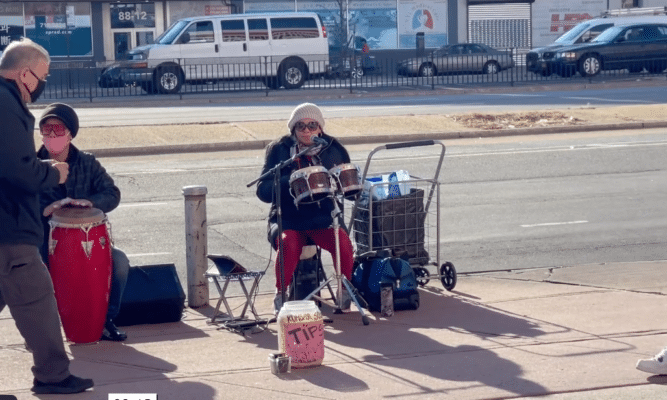 Musicians on Queens Boulevard and people passing by