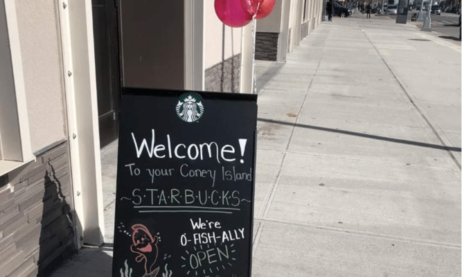 A sandwich board sign outside the new Starbucks saying: Welcome to your Coney Island Starbucks. We're o-fish-ally open!