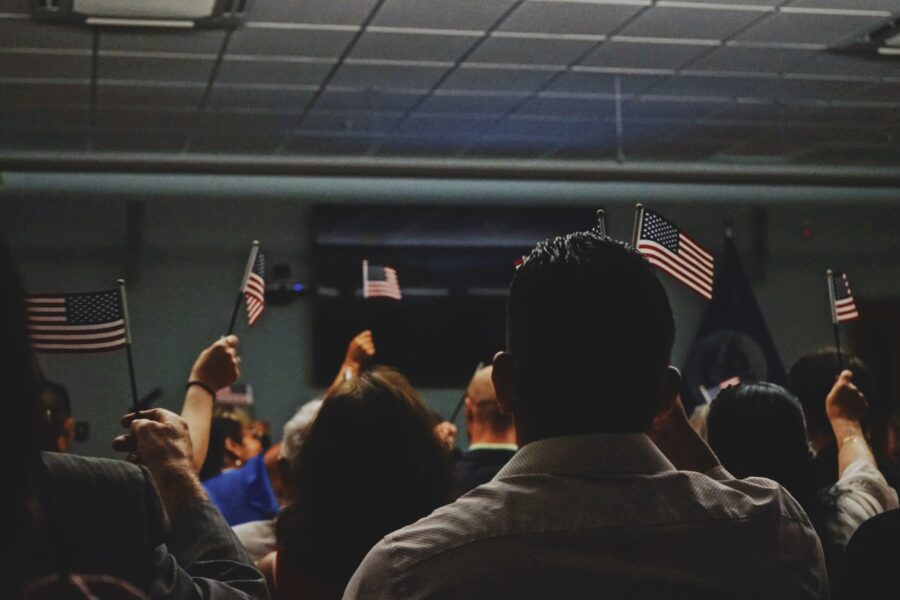 We see the backs of a room full of people who are holding miniature American flags.