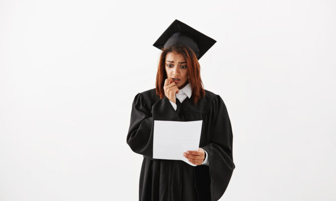 Sad displeased african female graduate in black mantle holding test over white background. Copy space.
