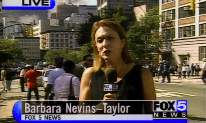 a screen grab of Barbara Nevins Taylor, a white reporter, reporting on 9/11/01. We see buildings and people and smoke behind her as she holds a mic and speaks to a camera as she's reporting.