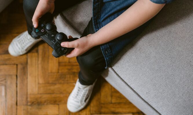 person-in-blue-denim-jeans-and-white-sneakers-sitting-on-gray-couch holding a gaming control