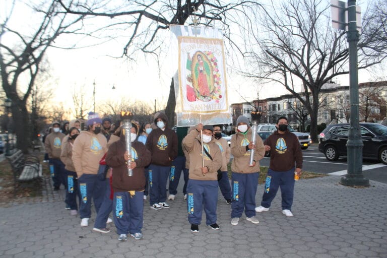 Parishioners walking in procession holding torches and the church banner.