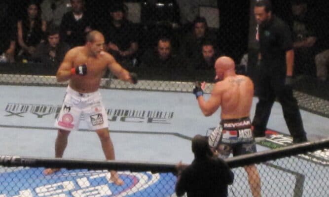 Two MMA fighters are in a match in a ring with a crowd behind them.