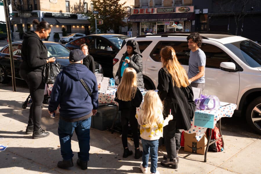 People line up at a table selling baked goods and raffles outside a polling place.