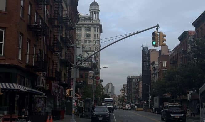 The corner of a NYC street in the lower east side with a somewhat busy street and an empty sidewalk.