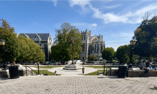 The City College of New York's nearly empty campus. An American flag hangs off the flagpole in the center frame. Shepard hall stands in the background.