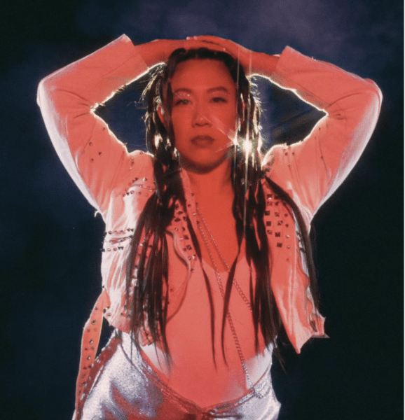 Yvonne Huatin Chow cast in red light and standing center frame, with both hands on top of her head.