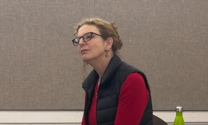 Filmmaker Deirdre Fishel against a brown background, looking to the left corner.