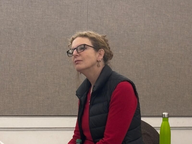 Filmmaker Deirdre Fishel against a brown background, looking to the left corner.