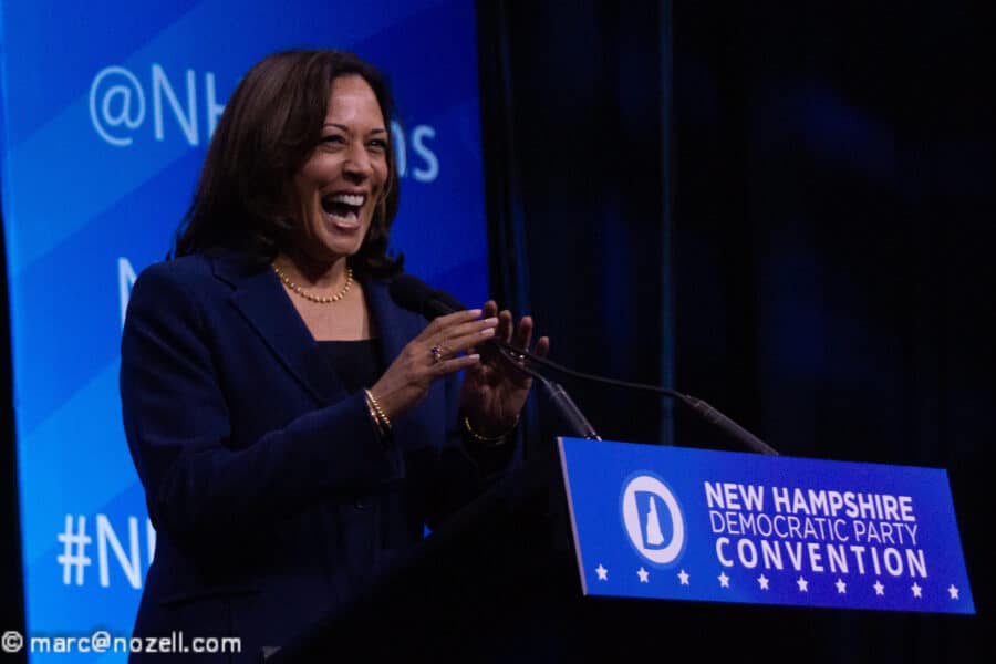 A smiling woman in a navy suit stands behind a blue podium.