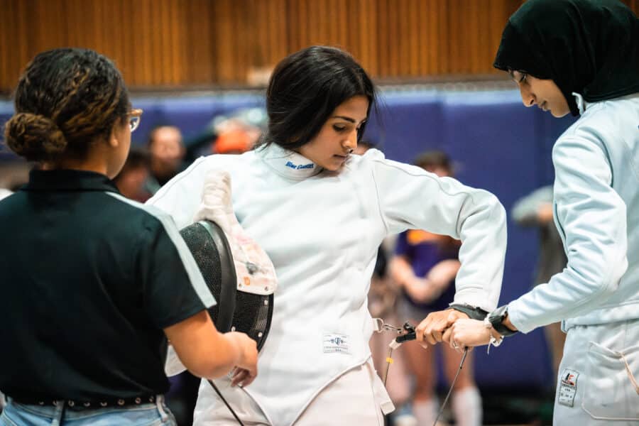 An Épée fencer prepares for her match with the help of her two teammates.