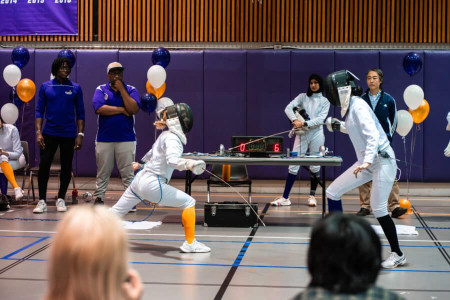 Two women fencers and one moves in to face the taller opponent