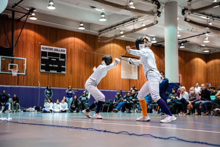 A female fencer lunges forward at her opponent during fencing match.