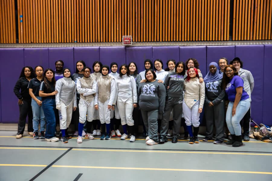 Women's fencing team and staff posing for a group photo in the gym.