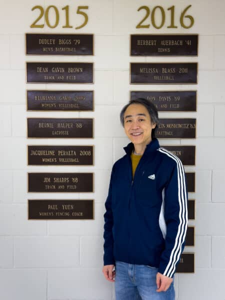 A man standing in-front of a wall with plaques displaying names and years.