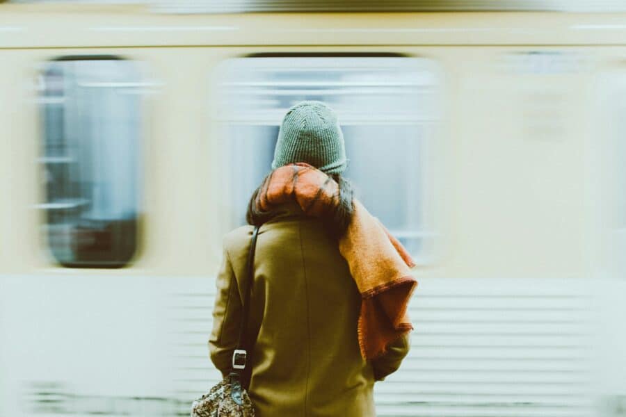 A woman in a hat and coat stands in beside a blurry, moving train car.