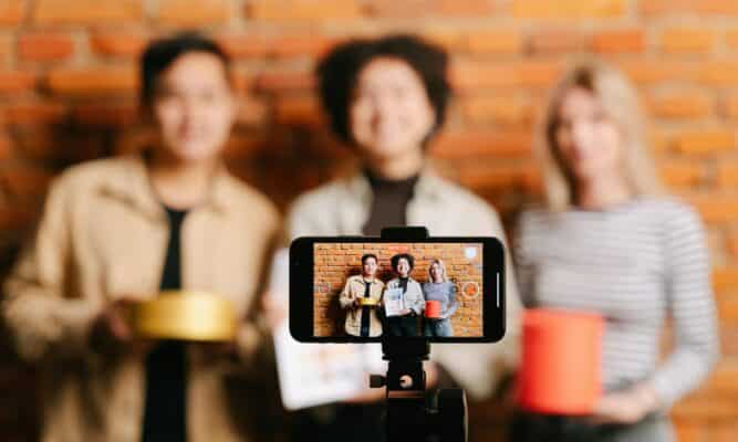 A camera on a tripod displays three people holding various products as is promoting them for an ad.