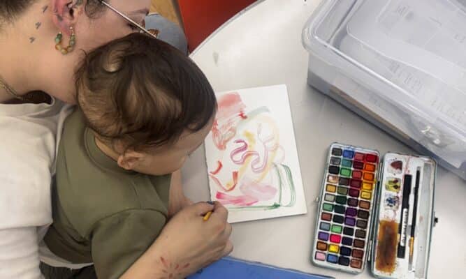 Woman holding baby in lap as they paint with watercolors.