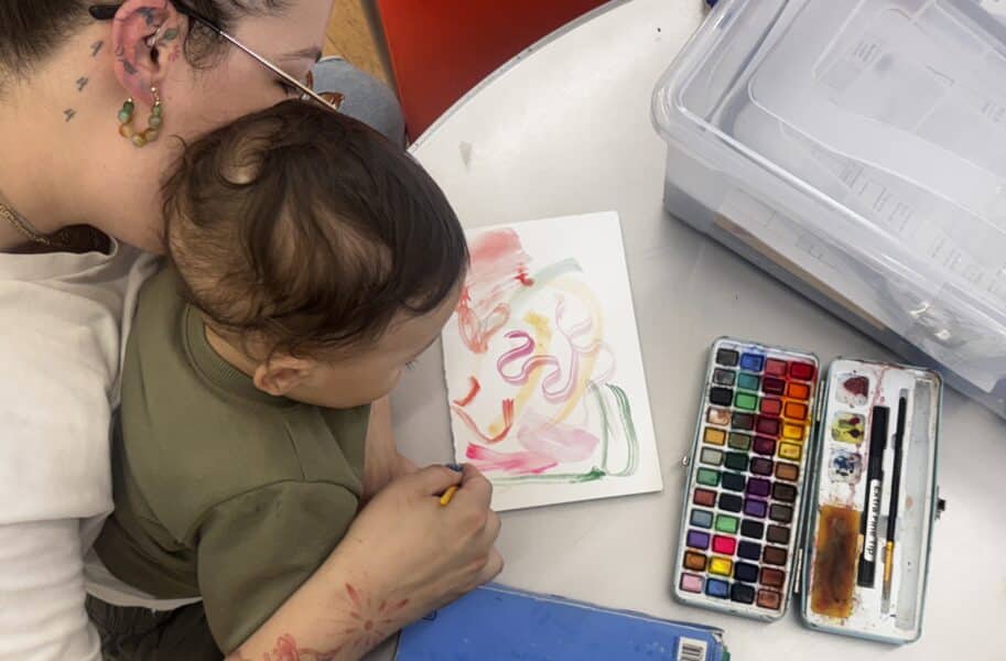 Woman holding baby in lap as they paint with watercolors.