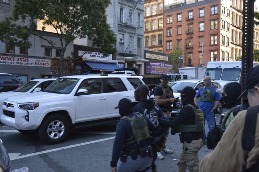 Masked federal agents escort a black man across the street in Chinatown, NYC.