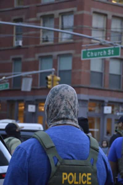 A masked federal agent faces away from the camera.