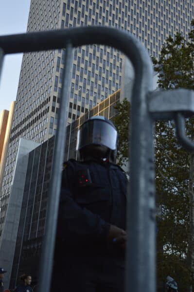 An NYPD officer in full protective gear with a lowered visor stationed behind a barricade