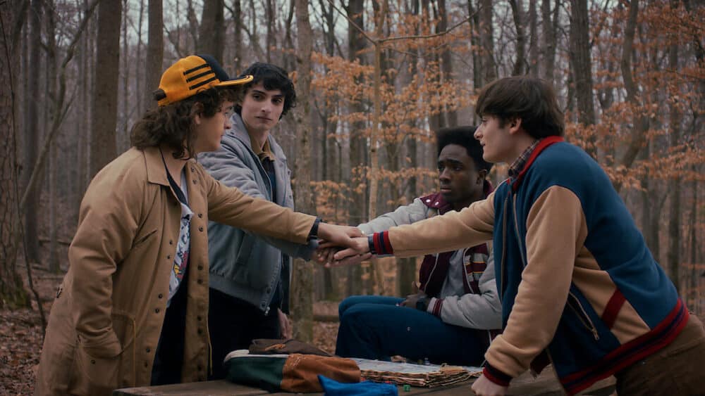 Four boys in the woods touching hands.
