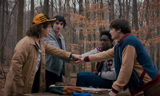 Four boys in the woods touching hands.