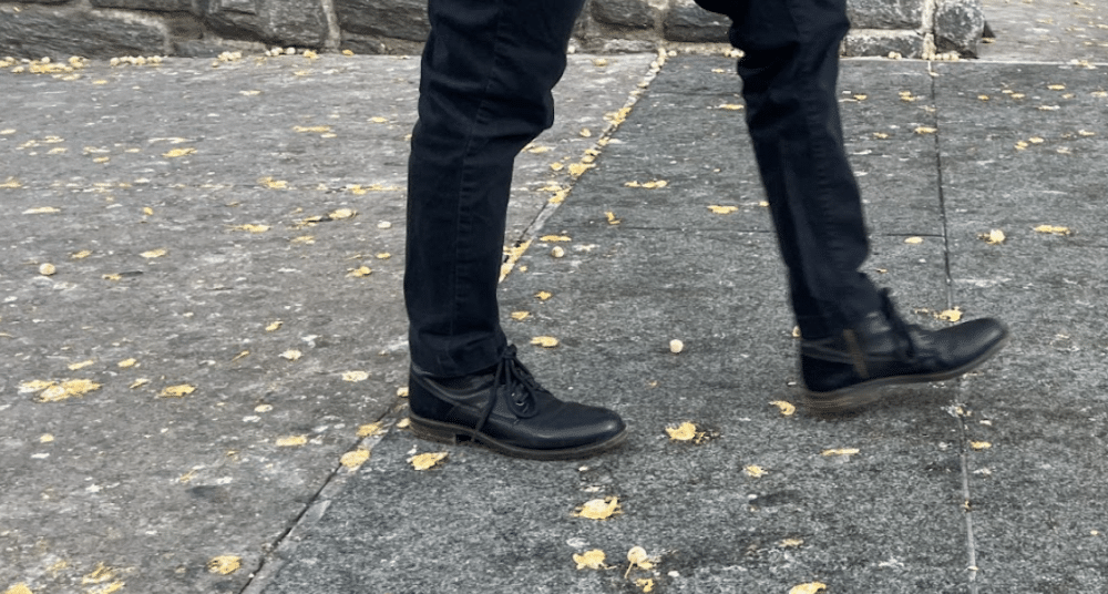 Person walking on a sidewalk filled with Gingko tree fruit on the floor