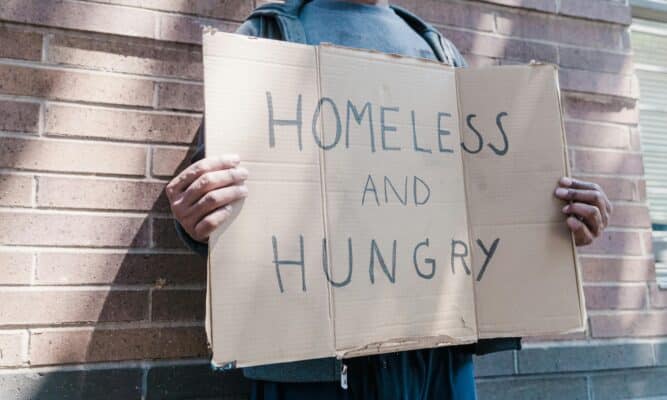 Man standing with homeless sign. Photo by Timur Weber.