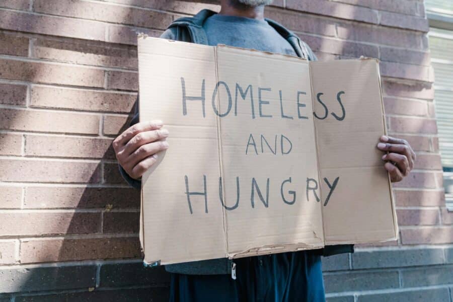 Man standing with homeless sign. Photo by Timur Weber.