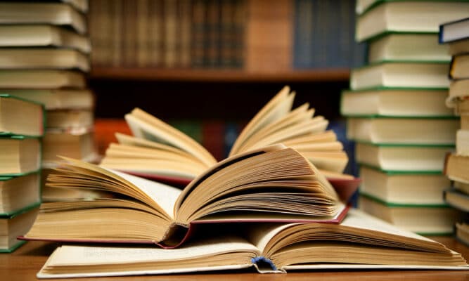 Stacks of books alongside a few open books.