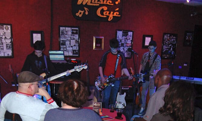 Crowded room of people 3 watching guitarists.
