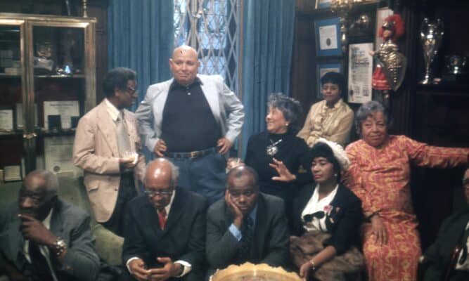 Still of the actors in Once Upon a Time in Harlem where the men and women pose together in an office decorated with framed certificates, awards and trophies.